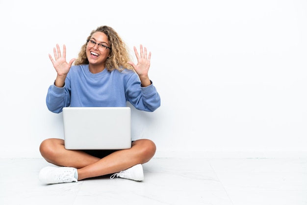 Menina com cabelo encaracolado com um laptop sentado no chão contando dez com os dedos