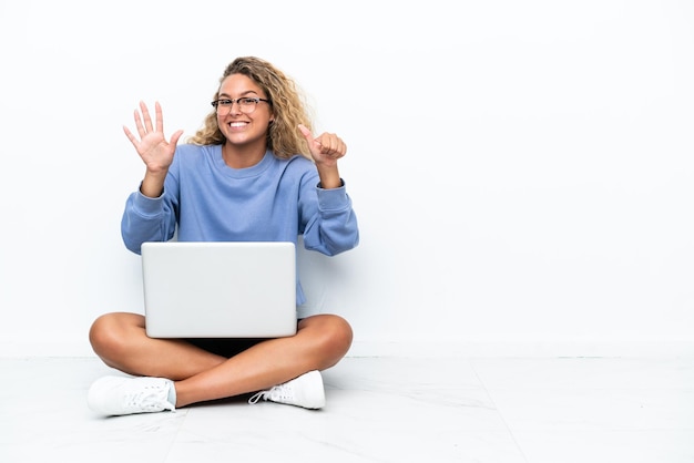Menina com cabelo encaracolado com um laptop sentado no chão contando seis com os dedos