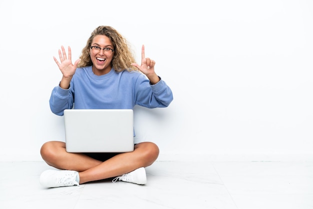 Menina com cabelo encaracolado com um laptop sentado no chão contando sete com os dedos