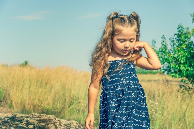 Foto menina com cabelo encaracolado em um vestido azul contra um céu azul ensolarado. criança na natureza. bandeira