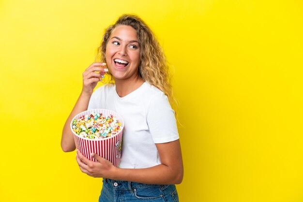 Menina com cabelo encaracolado isolado em um fundo amarelo segurando um grande balde de pipocas