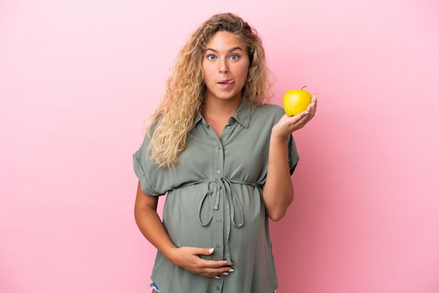 Menina com cabelo encaracolado isolado em um fundo rosa grávida e segurando uma maçã