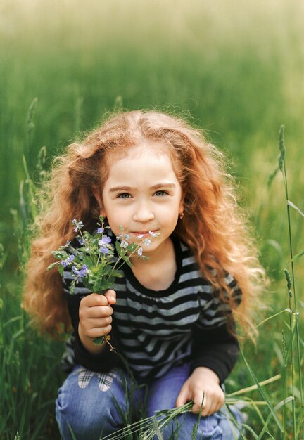 Menina com cabelo encaracolado no parque com um buquê de flores silvestres. fechar-se. vertical