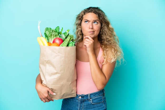 Menina com cabelo encaracolado, segurando uma sacola de compras isolada em fundo verde, tendo dúvidas e pensando