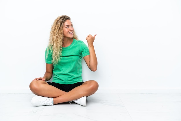 Menina com cabelo encaracolado sentada no chão apontando para o lado para apresentar um produto