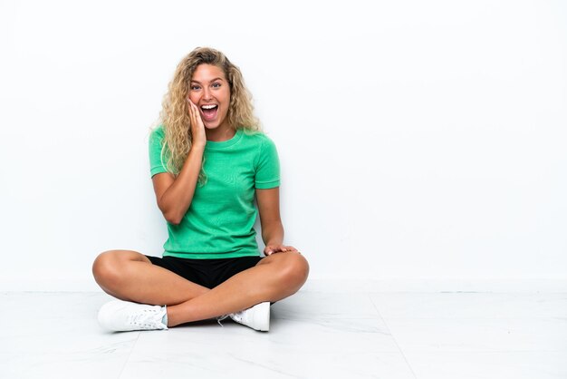 Menina com cabelo encaracolado sentada no chão com expressão facial de surpresa e choque