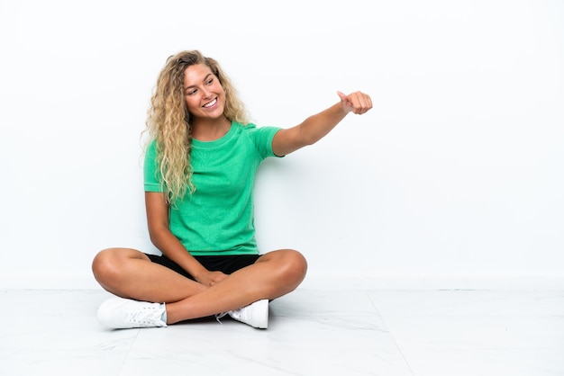 Menina com cabelo encaracolado sentada no chão dando um polegar para cima gesto