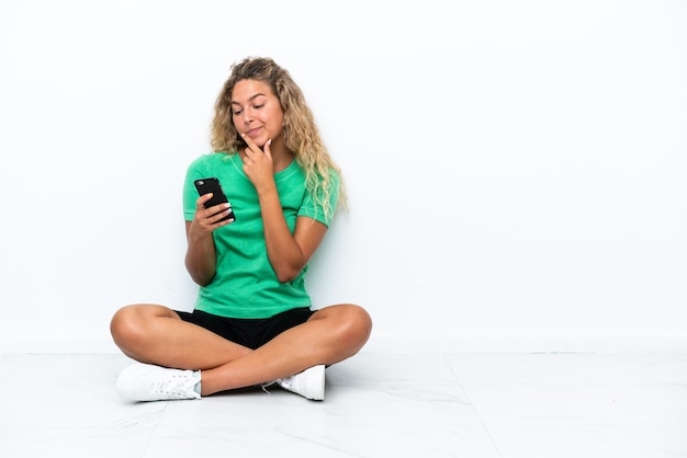 Menina com cabelo encaracolado sentada no chão pensando e enviando uma mensagem