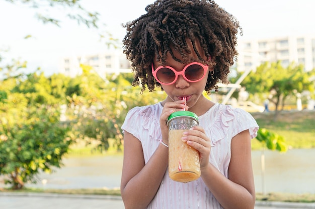 Menina com cabelo encaracolado tomando uma bebida saudável no parque