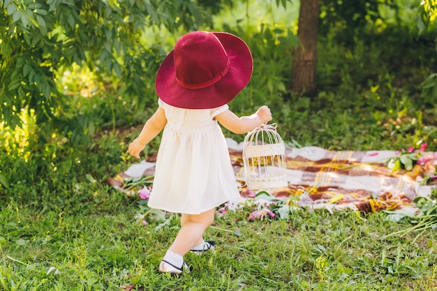 menina com cabelo loiro em um vestido branco e chapéu vermelho da mãe no parque ensolarado dia de verão