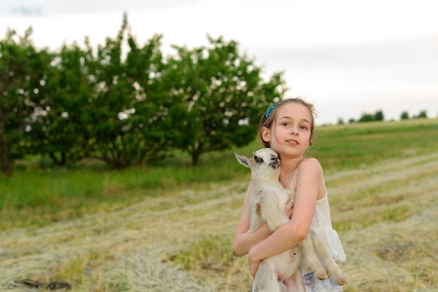 Menina com cabra bebê na fazenda ao ar livre. Amor e cuidado. Animais da aldeia. criança feliz abraça cabra