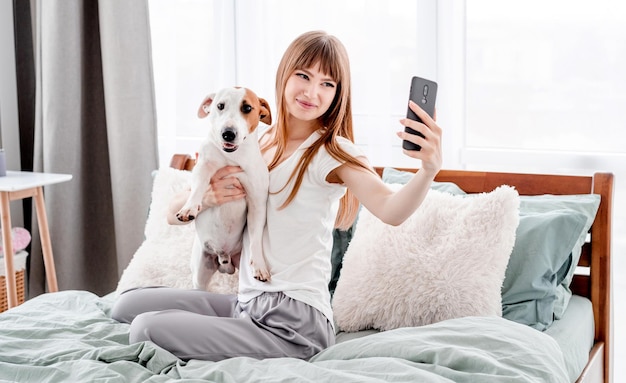 Menina com cachorro e smartphone na cama