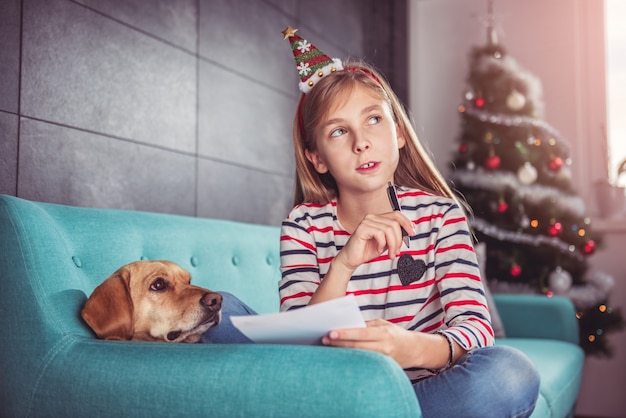 Menina com cachorro escrevendo a lista de desejos no sofá