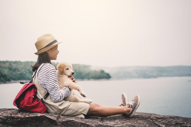 Foto menina com cachorro sentado em uma rocha à beira do lago contra o céu