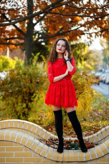 Menina com cachos em um vestido vermelho em um beco no outono