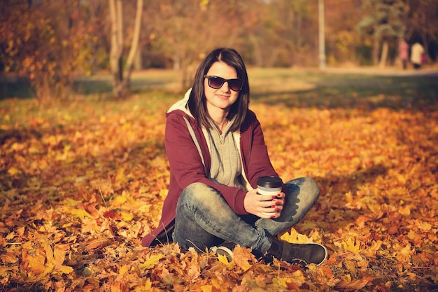 Menina com café sentado em folhas amarelas