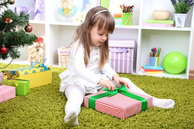 Menina com caixa de presente perto da árvore de natal na sala