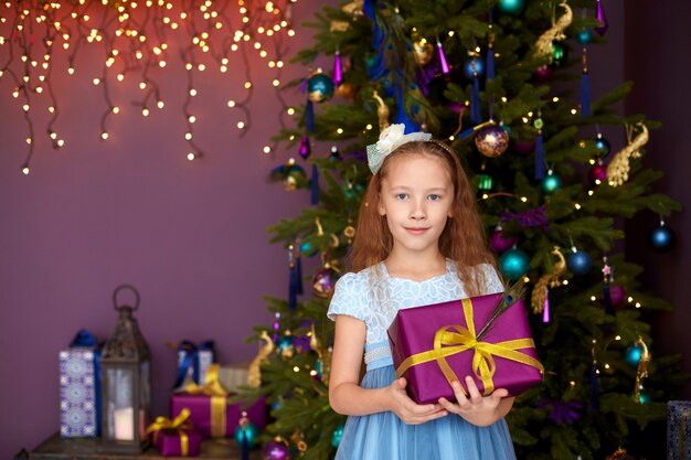 Menina com caixa de presente perto de árvore de Natal