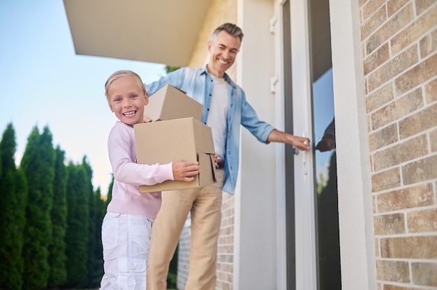 Menina com caixa e pai entrando em casa