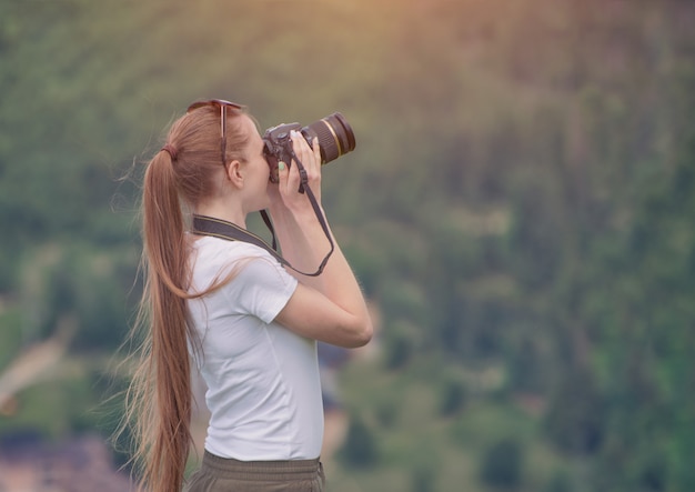 Menina com câmera fica em uma colina e fotografar a natureza. Floresta no fundo