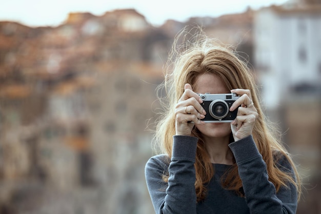 Menina com câmera retro falando fotos ao ar livre, itália, pitigliano. toscana