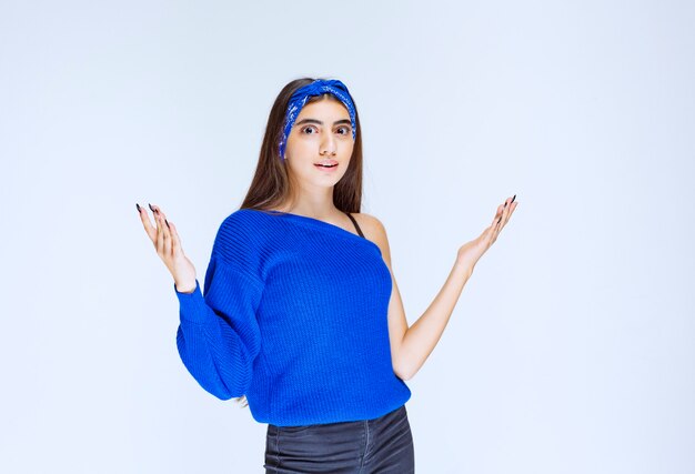 Menina com camisa de festa azul, apresentando algo acima.