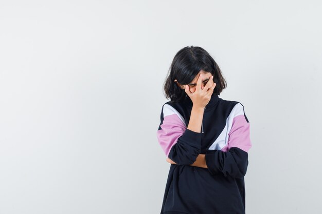 Menina com camisa, segurando a mão no rosto e parecendo feliz, vista frontal.