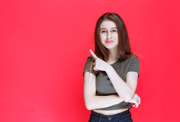 Menina com camisa verde, mostrando algo no oeste.