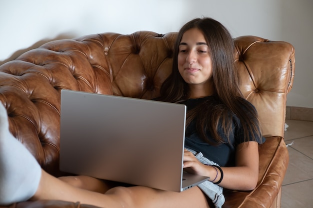 Menina com cara engraçada segurando um laptop em um sofá de couro de luxo. Conceito útil para personalização