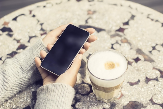 Menina com celular em branco e xícara de café