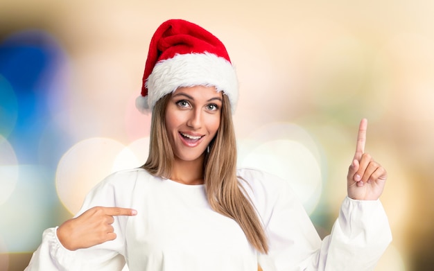 Menina com chapéu de Natal com expressão facial de surpresa sobre parede fora de foco