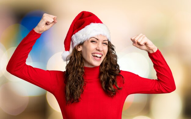 Menina com chapéu de Natal comemorando uma vitória sobre parede fora de foco