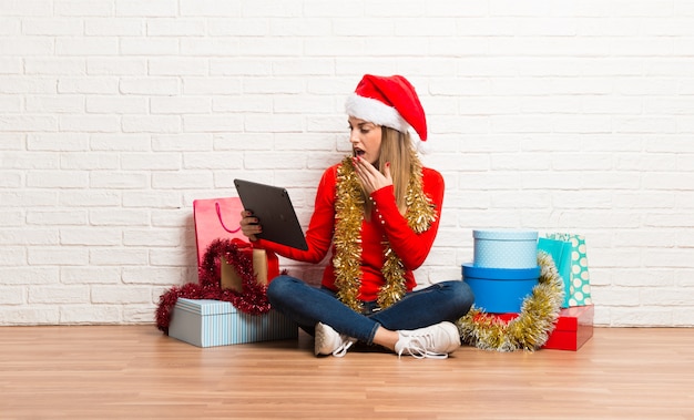 Menina com chapéu de natal e muitos presentes comemorando as férias de natal com um tablet