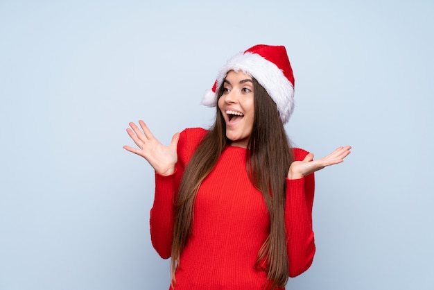 Menina com chapéu de Natal isolado azul com expressão facial de surpresa