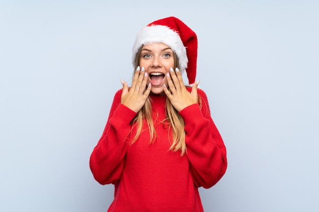 Menina com chapéu de Natal isolado parede azul com expressão facial de surpresa