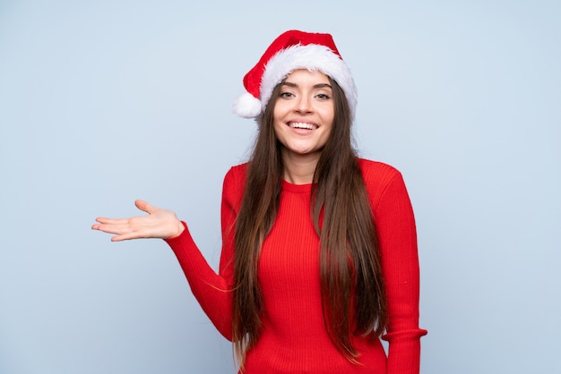 Menina com chapéu de natal sobre azul isolado segurando copyspace imaginário na palma da mão