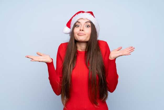 Menina com chapéu de natal sobre azul isolado, tendo dúvidas e com a expressão do rosto confuso