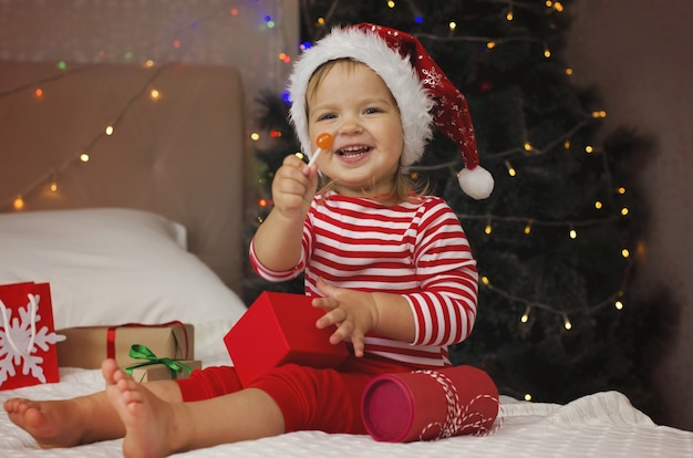 Foto menina com chapéu de papai noel abrindo caixa de presente de natal criança divertida e expressiva curtindo os presentes