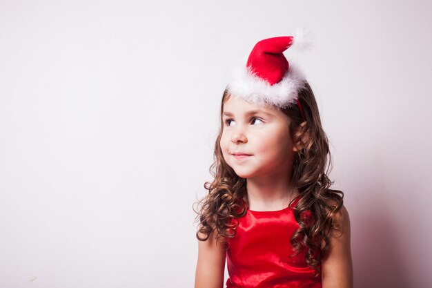 Menina com chapéu de Papai Noel na cabeça sobre uma parede branca, copie o espaço