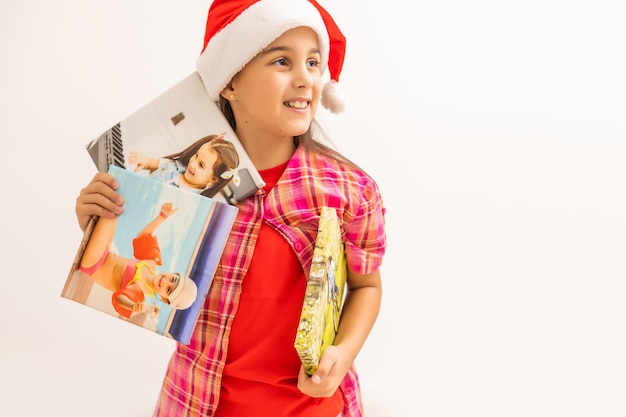 Menina com chapéu de Papai Noel sorrindo e segurando a tela de fotos na mão. Conceito de Natal. Copie o espaço.