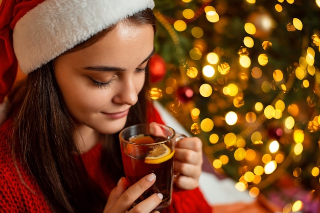 Menina com chapéu de Papai Noel vermelho com uma xícara de chá de chocolate