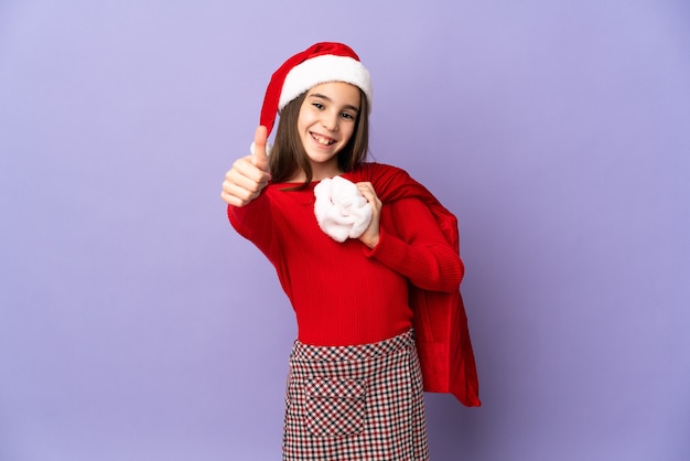 Menina com chapéu e saco de Natal isolado na parede roxa com polegar para cima porque algo bom aconteceu