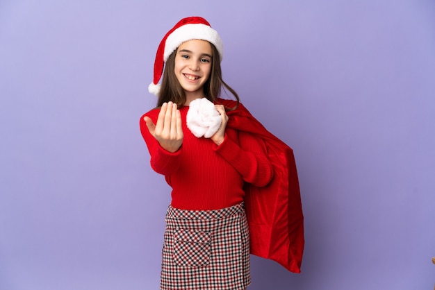 Menina com chapéu e saco de Natal isolado na parede roxa convidando para vir com a mão