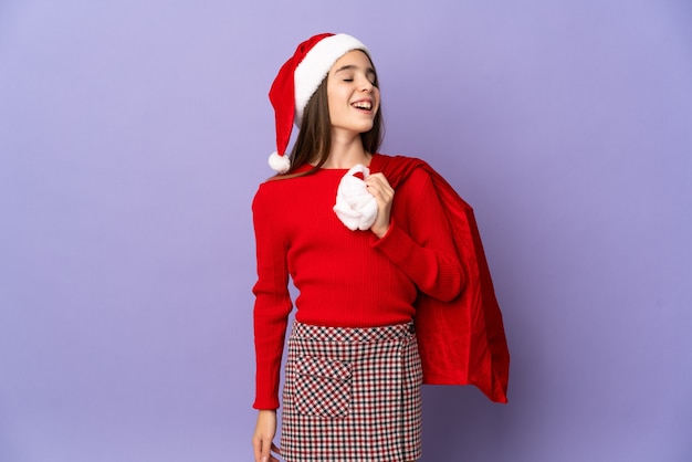 Menina com chapéu e saco de Natal isolado no fundo roxo rindo
