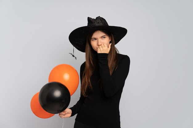 Menina com chapéu preto e vestido preto segurando balões