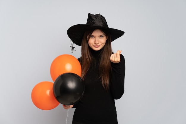 Menina com chapéu preto e vestido preto segurando balões