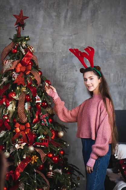 Menina com chifres de veado no fundo da árvore de Natal.