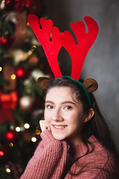 Foto menina com chifres de veado no fundo da árvore de natal.