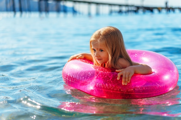 Menina com círculo inflável rosa tomando banho no mar