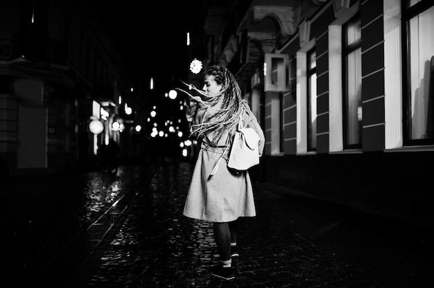 Menina com dreadlocks andando na rua à noite da cidade.